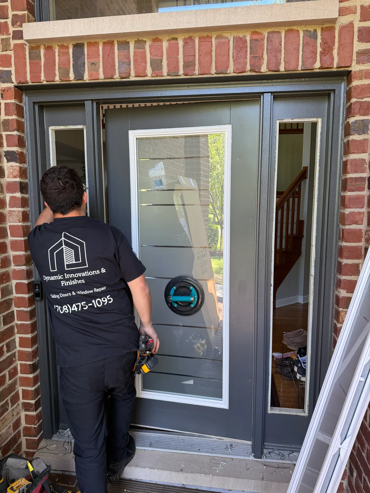Technician setting insulated glass in a dark entry door with sidelights, suction cup on the panel